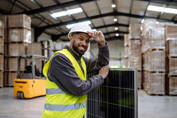 Handsome worker carrying solar panel in warehouse or factory. Solar panel manufacturer, solar manufacturing.