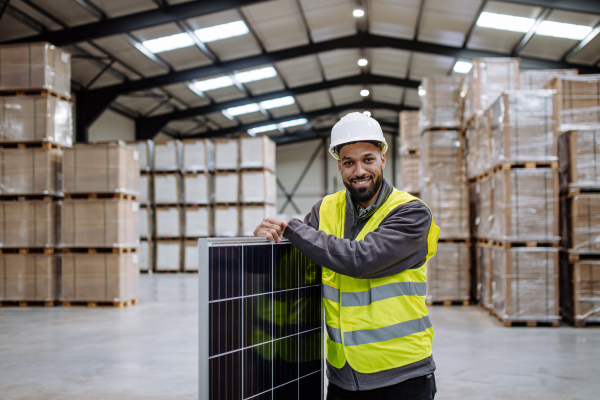 Handsome worker carrying solar panel in warehouse or factory. Solar panel manufacturer, solar manufacturing.