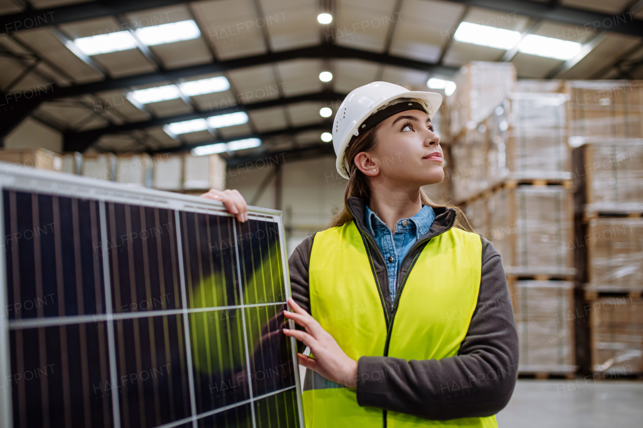 Female worker carrying solar panel in warehouse or factory. Solar panel manufacturer, solar manufacturing.