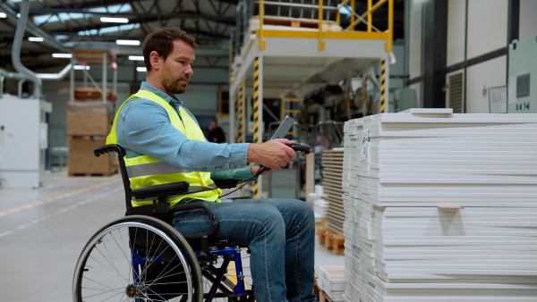 Man in wheelchair working in modern industrial factory, in adjustable workstation. Concept of workers with disabilities, accessible workplace for employees with mobility impairment.