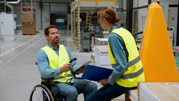 Video of man in wheelchair working in warehouse, talking with colleague. Concept of workers with disabilities, accessible workplace for employees with mobility impairment.