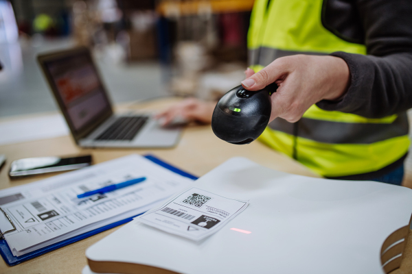 Female warehouse worker holding scanner and scanning the barcodes on products in warehouse, checking in laptop. Warehouse manager using warehouse scanning system.