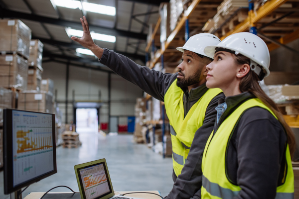 Warehouse manager talking with logistics employee in warehouse, planning transport of products, goods, talking shipping process.