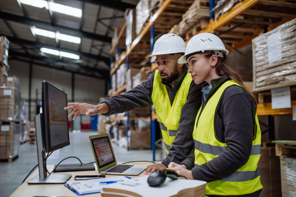 Warehouse manager talking with logistics employee in warehouse, planning transport of products, goods, talking shipping process.