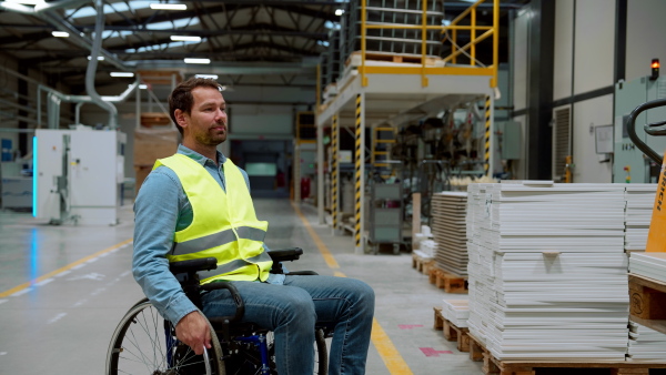 Man in wheelchair working in modern industrial factory, in adjustable workstation. Concept of workers with disabilities, accessible workplace for employees with mobility impairment.