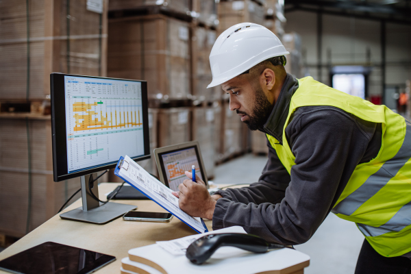 Portrait of warehouseman checking delivery, stock in warehouse on company pc, computer. Warehouse manager using warehouse management software, app.