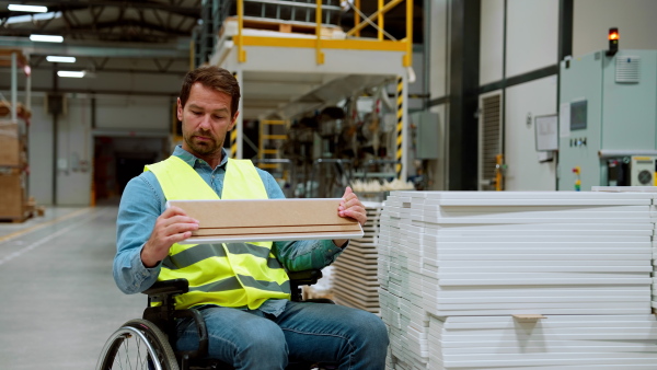 Man in wheelchair working in modern industrial factory, in adjustable workstation. Concept of workers with disabilities, accessible workplace for employees with mobility impairment.