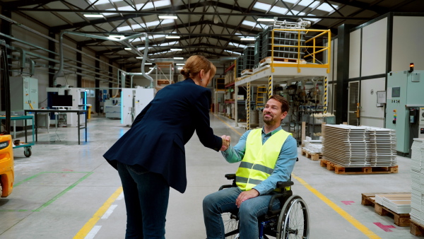 Man in wheelchair working in warehouse, shaking hand with HR manager, director. Concept of workers with disabilities, accessible workplace for employees with mobility impairment.