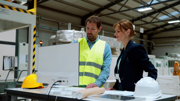 Female engineer reading technical documentation with project manager in modern industrial factory, talking about new production project or investment. Team management in the manufacturing facility.