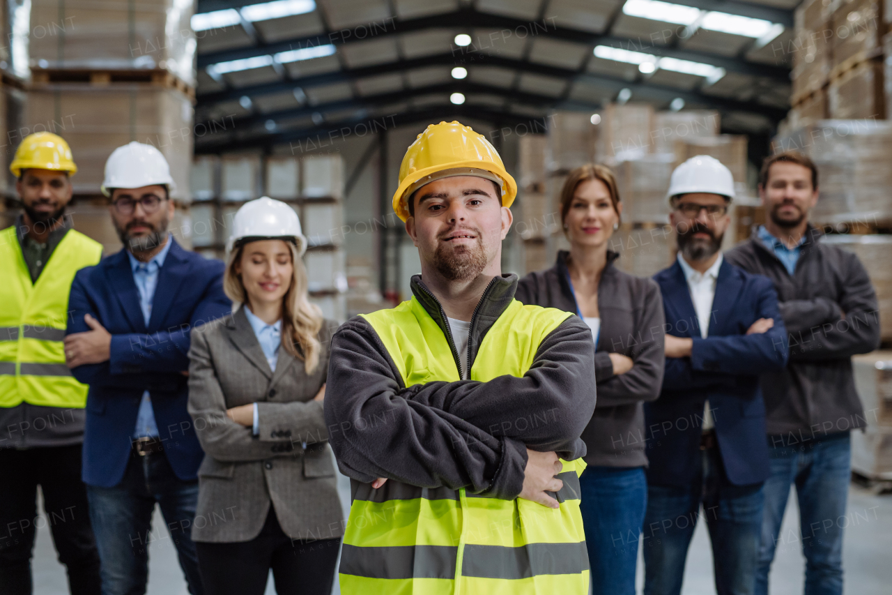 Full team of warehouse employees standing in warehouse. Team of workers, managers and female director, and worker with down syndrome in modern industrial factory, heavy industry, manufactrury. Group portrait.