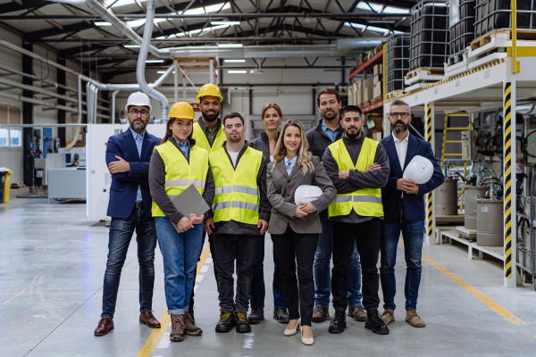 Full team of warehouse employees standing in warehouse. Team of workers, managers and female director in modern industrial factory, heavy industry, manufactrury. Group portrait.