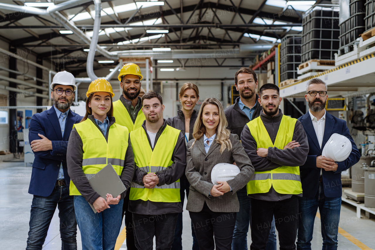 Full team of warehouse employees standing in warehouse. Team of workers, managers and female director, and worker with down syndrome in modern industrial factory, heavy industry, manufactrury. Group portrait.