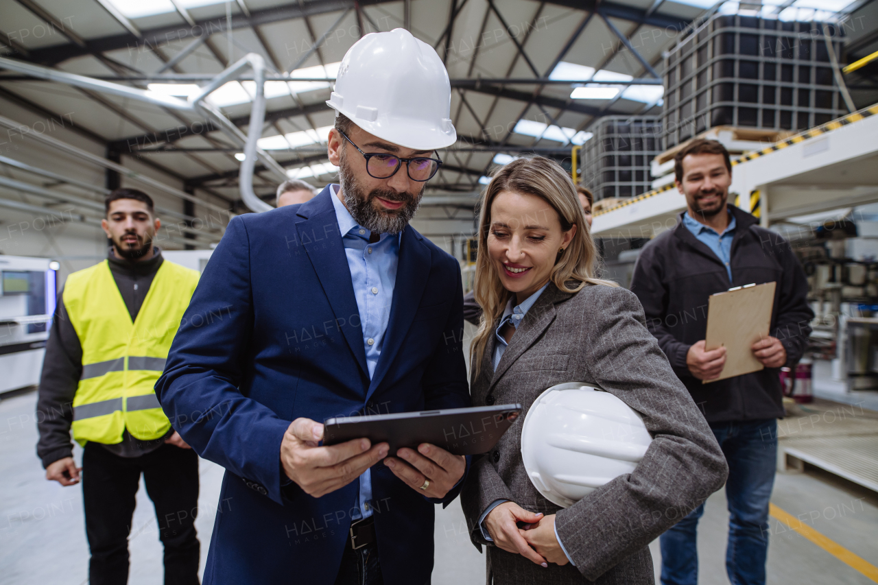 Full team of warehouse employees walking in warehouse, looking at tablet. Team of workers, managers and female director in modern industrial factory, heavy industry, manufactrury. Group portrait.