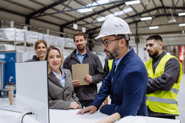 Manager presenting project to the full team of warehouse employees on computer. Team of workers, managers, female director in modern industrial factory, heavy industry, manufactrury.