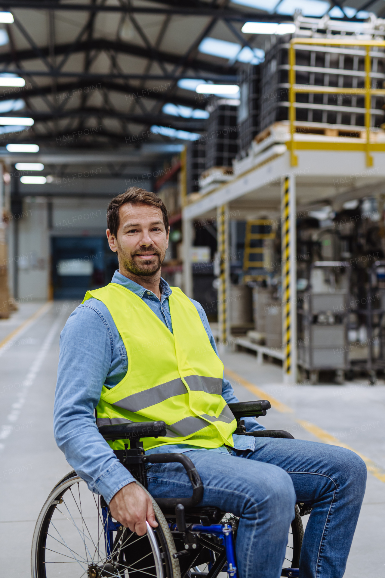 Man in wheelchair working in modern industrial factory. Concept of workers with disabilities, accessible workplace for employees with mobility impairment.