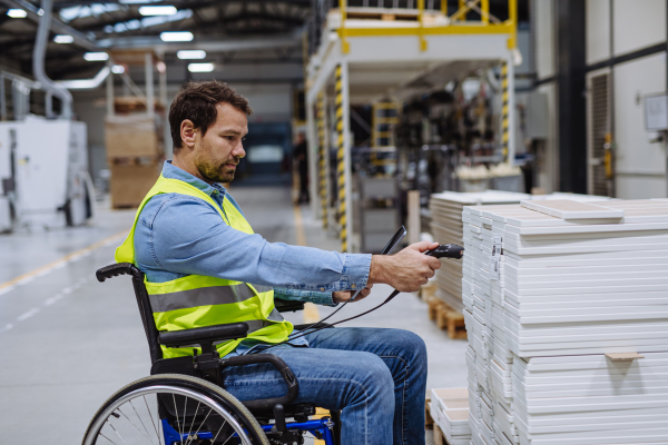 Man in wheelchair working in modern industrial factory, scanning barcodes with scanner. Concept of workers with disabilities, accessible workplace for employees with mobility impairment.