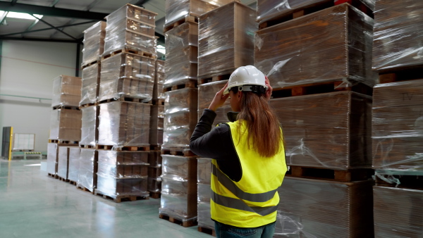 Video of female warehouse worker standing in warehouse. Warehouse employee putting on a working helmet. Vertical view.