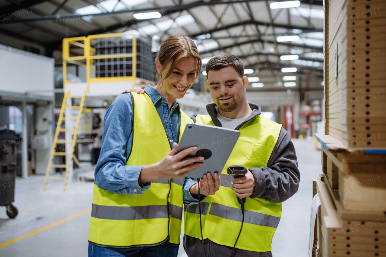 Young man with Down syndrome working in warehouse, female colleague teaching him how to scan products with scanner. Concept of workers with disabilities, support in workplace.