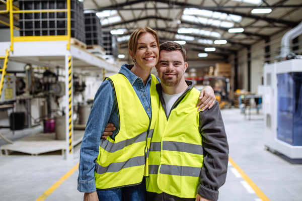 Young man with Down syndrome working in warehouse, colleague talking with him. Concept of the workers with disabilities, support in workplace.