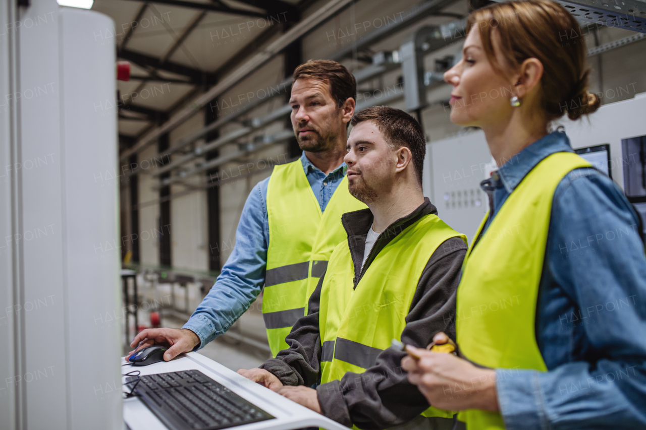 Young man with Down syndrome working in warehouse, colleague teaching him how to work with computer. Concept of workers with disabilities, support in workplace.