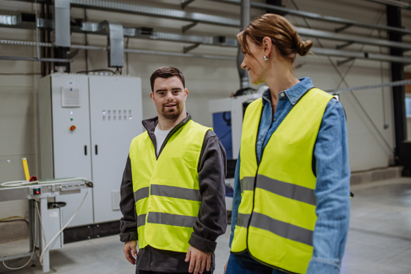 Young man with Down syndrome working in warehouse, colleague talking with him. Concept of the workers with disabilities, support in workplace.