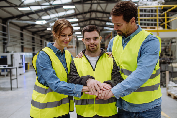 Young man with Down syndrome working in warehouse, colleague teaching him how to work with computer. Concept of workers with disabilities, support in workplace.