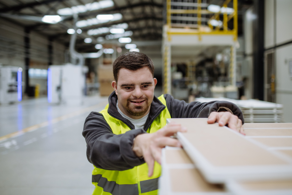 Young man with Down syndrome working in warehouse. Concept of workers with disabilities, support in workplace.