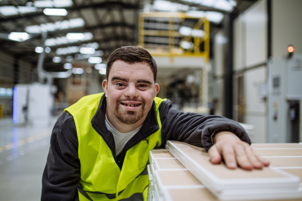 Young man with Down syndrome working in warehouse. Concept of workers with disabilities, support in workplace.