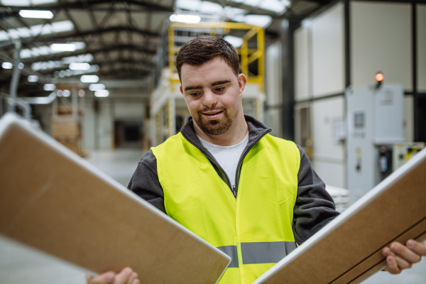 Young man with Down syndrome working in warehouse. Concept of workers with disabilities, support in workplace.