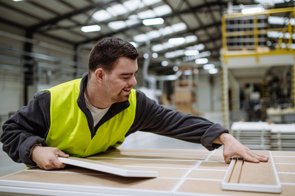 Young man with Down syndrome working in warehouse. Concept of workers with disabilities, support in workplace.