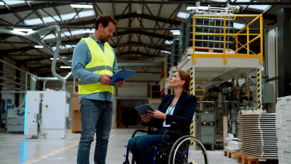 Video of female manager, director in wheelchair working in warehouse, talking with logistics employee. Concept of workers with disabilities, accessible workplace for employees with mobility impairment.