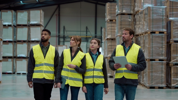 Front view of warehouse workers in reflective vest walking in warehouse. Team of warehouse workers preparing products for shipment.