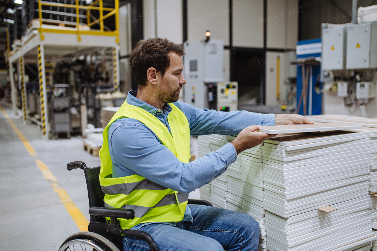 Man in wheelchair working in modern industrial factory, scanning barcodes with scanner. Concept of workers with disabilities, accessible workplace for employees with mobility impairment.