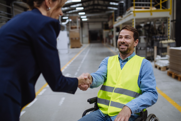 Man in wheelchair working in warehouse, shaking hand with HR manager, director. Concept of workers with disabilities, accessible workplace for employees with mobility impairment.