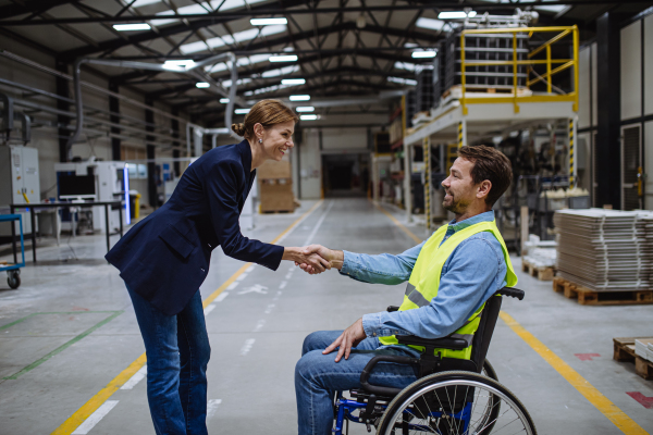 Man in wheelchair working in warehouse, shaking hand with HR manager, director. Concept of workers with disabilities, accessible workplace for employees with mobility impairment.