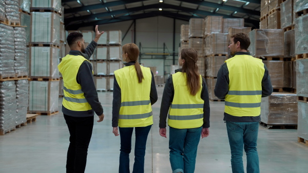 Rear view of warehouse workers in reflective vest walking in warehouse. Team of warehouse workers preparing products for shipment.