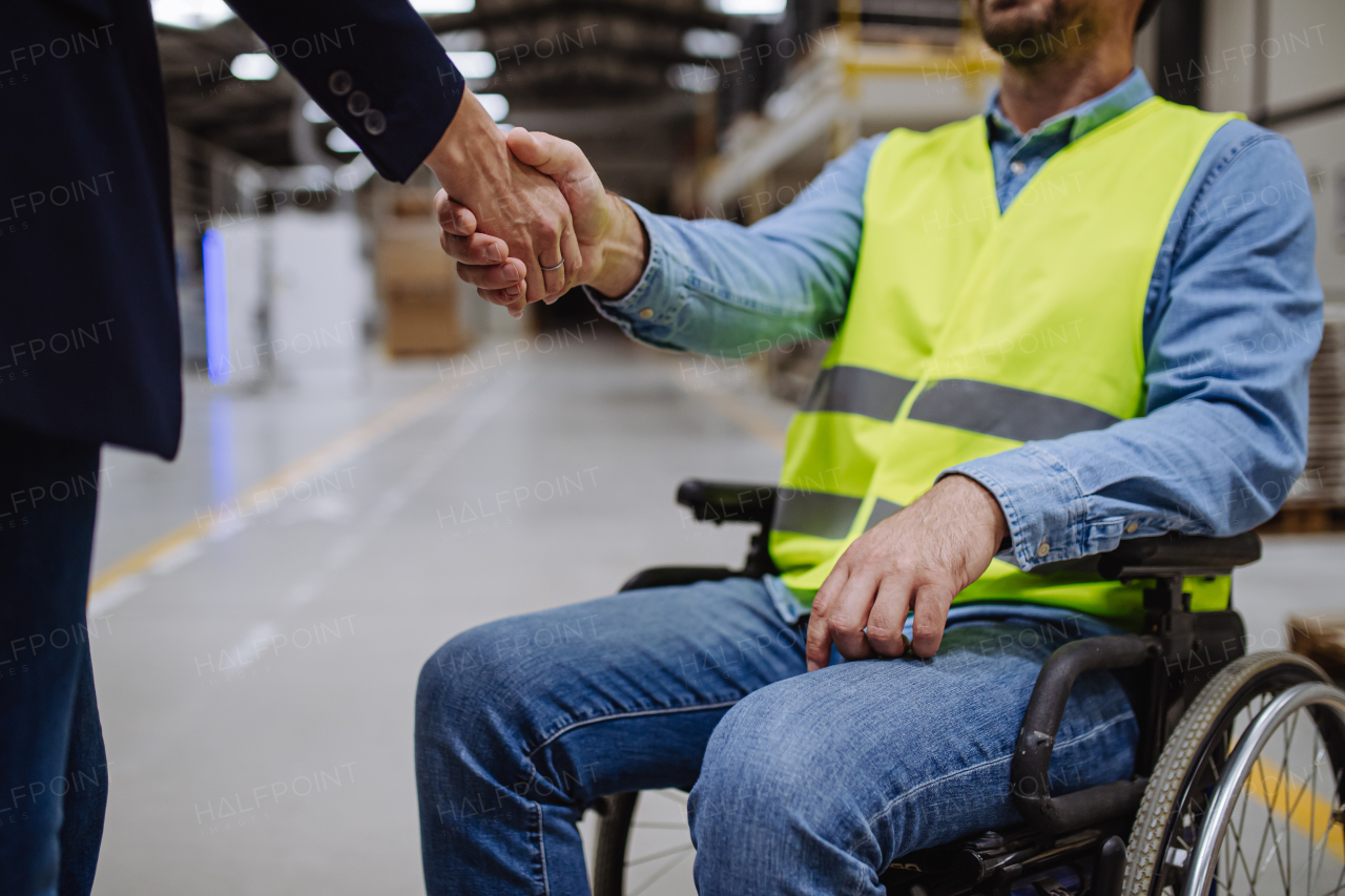 Man in wheelchair working in warehouse, shaking hand with HR manager, director. Concept of workers with disabilities, accessible workplace for employees with mobility impairment.