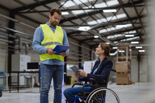 Portrait of female manager, director in wheelchair working in warehouse, talking with logistics employee. Concept of workers with disabilities, accessible workplace for employees with mobility impairment.