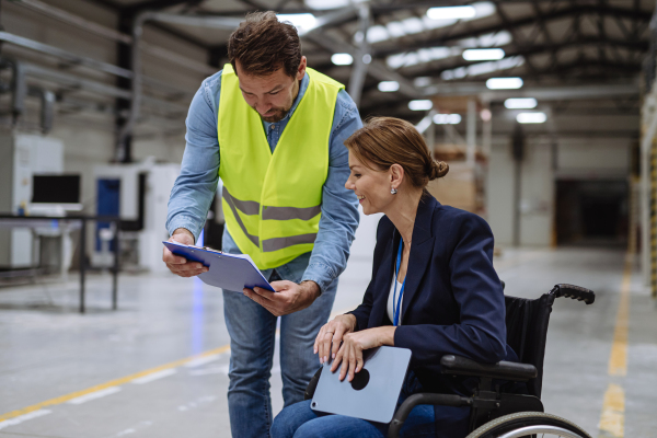 Portrait of female manager, director in wheelchair working in warehouse, talking with logistics employee. Concept of workers with disabilities, accessible workplace for employees with mobility impairment.