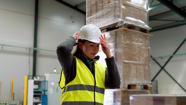 Video of female warehouse worker standing in warehouse. Warehouse employee putting on a working helmet. Vertical view.