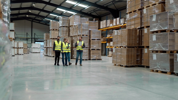 Front view of warehouse workers in reflective vest walking in warehouse. Team of warehouse workers preparing products for shipment.