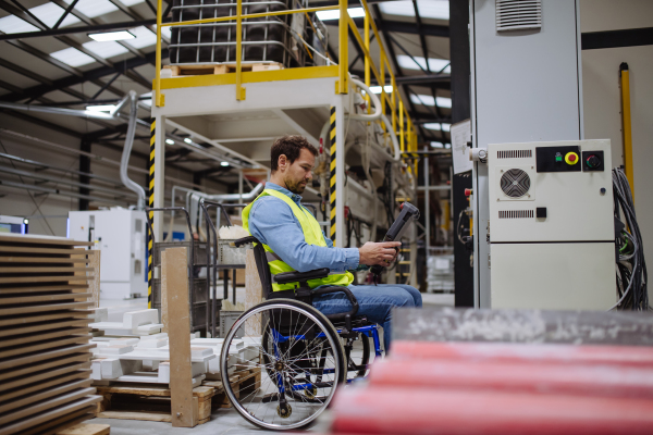 Man in wheelchair working in modern industrial factory, in adjustable workstation. Concept of workers with disabilities, accessible workplace for employees with mobility impairment.