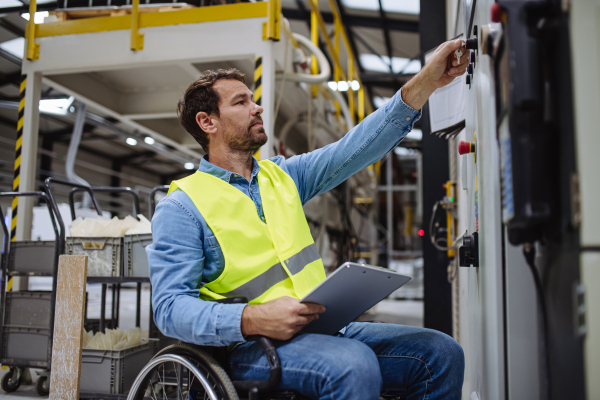 Man in wheelchair working in modern industrial factory, in adjustable workstation. Concept of workers with disabilities, accessible workplace for employees with mobility impairment.