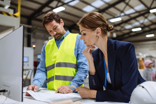 Female warehouse director talking with production manager, discussing new order, preparing products for shipment, delivery, checking stock in the warehouse.