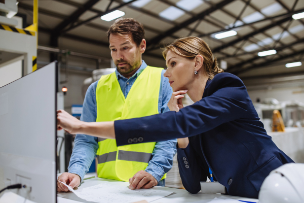 Female engineer reading technical documentation with project manager in modern industrial factory, talking about new production project or investment. Team management in the manufacturing facility.