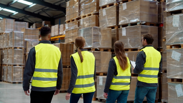 Rear view of warehouse workers in reflective vest walking in warehouse. Team of warehouse workers preparing products for shipment.