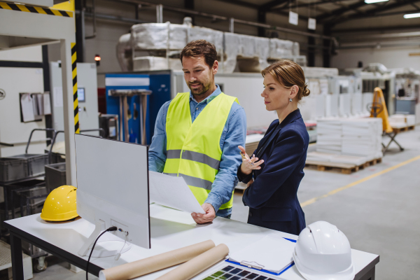 Female engineer reading technical documentation with project manager in modern industrial factory, talking about new production project or investment. Team management in the manufacturing facility.