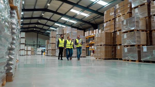 Front view of warehouse workers in reflective vest walking in warehouse. Team of warehouse workers preparing products for shipment.