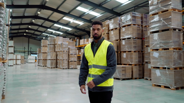 Video of male warehouse worker standing in warehouse. Warehouse manager checking delivery, stock in warehouse, inspecting products for shipment.