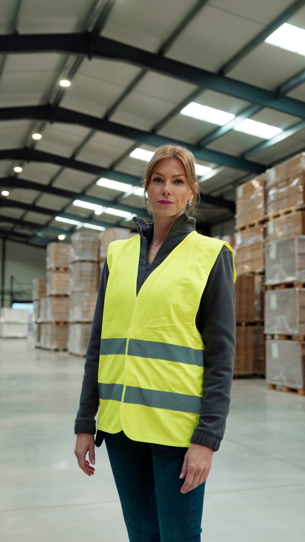 Video of female warehouse worker standing in warehouse. Warehouse manager checking delivery, stock in warehouse, inspecting products for shipment. Vertical view.